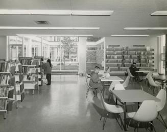 Picture of interior of library showing tables and shelves and large window to courtyard. 