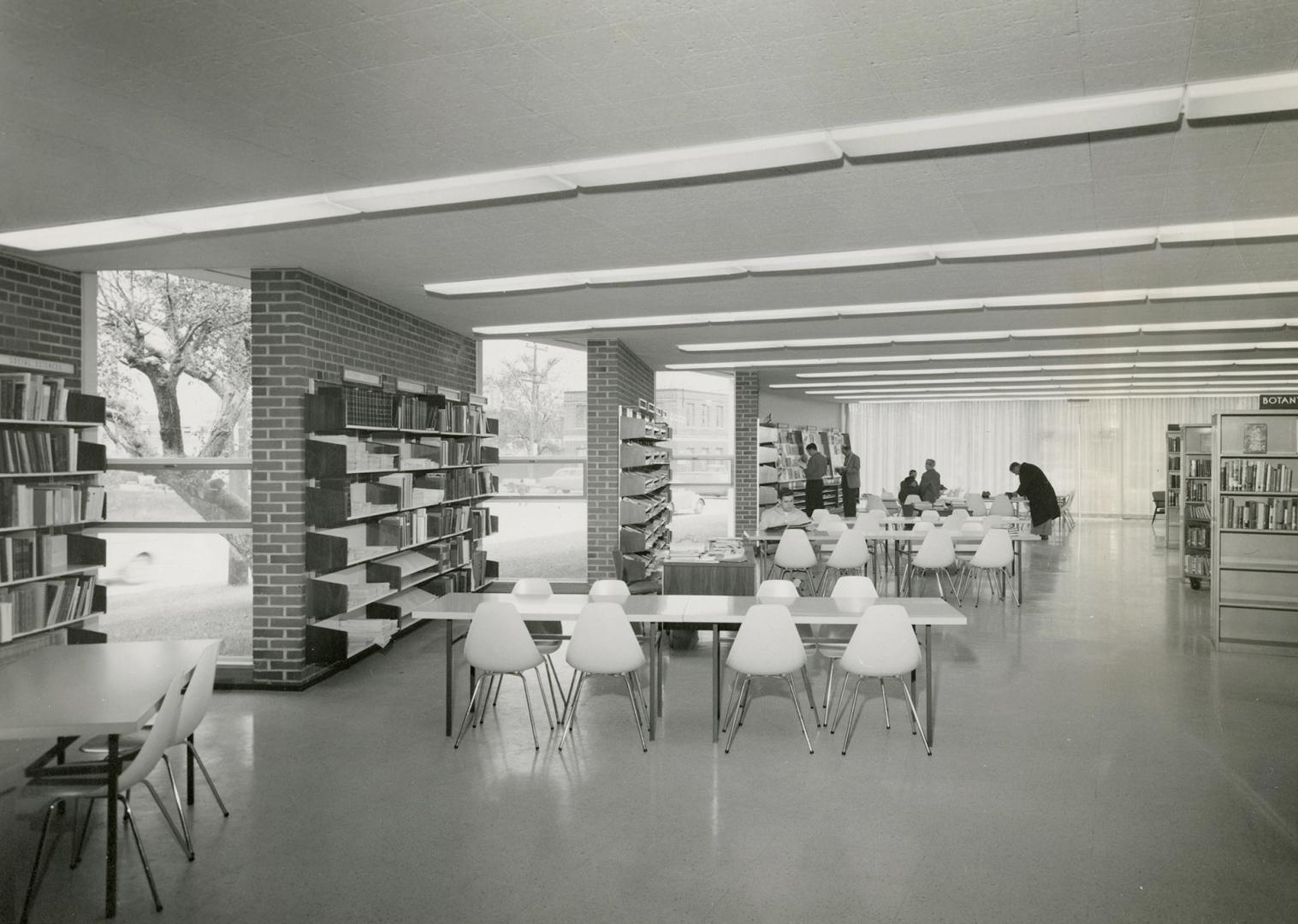 Picture of interior of library showing tables and shelves and large windows. 