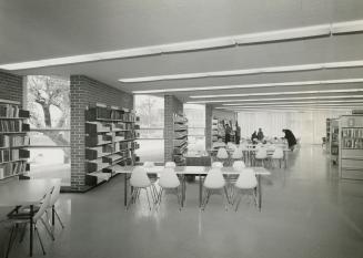 Picture of interior of library showing tables and shelves and large windows. 
