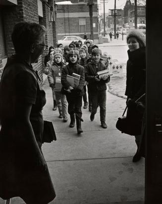 Picture of a group of children coming from outside into a library with librarian greeting them …