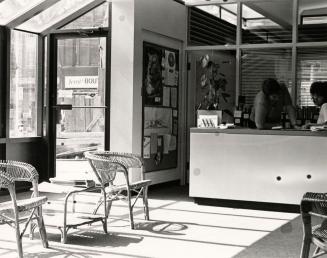 Picture of the interior of a library with reference desk and two wicker chairs and exterior doo…