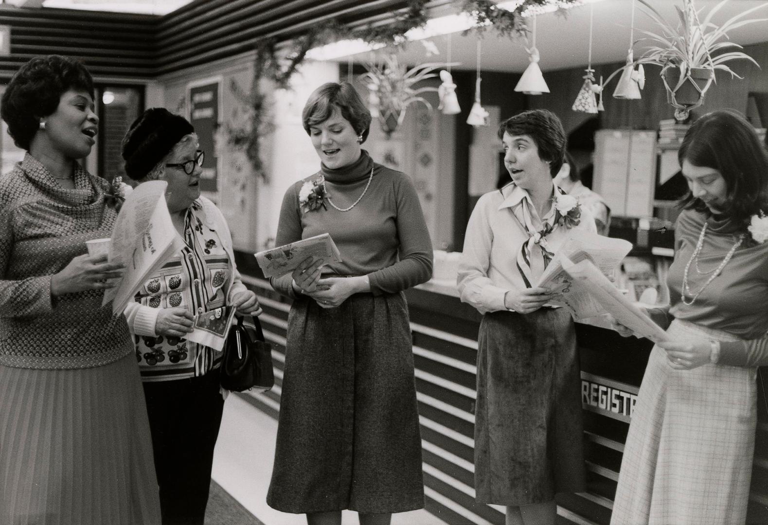 Picture of four staff standing singing in front of registration desk in a library. 