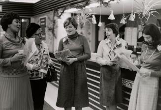 Picture of four staff standing singing in front of registration desk in a library. 