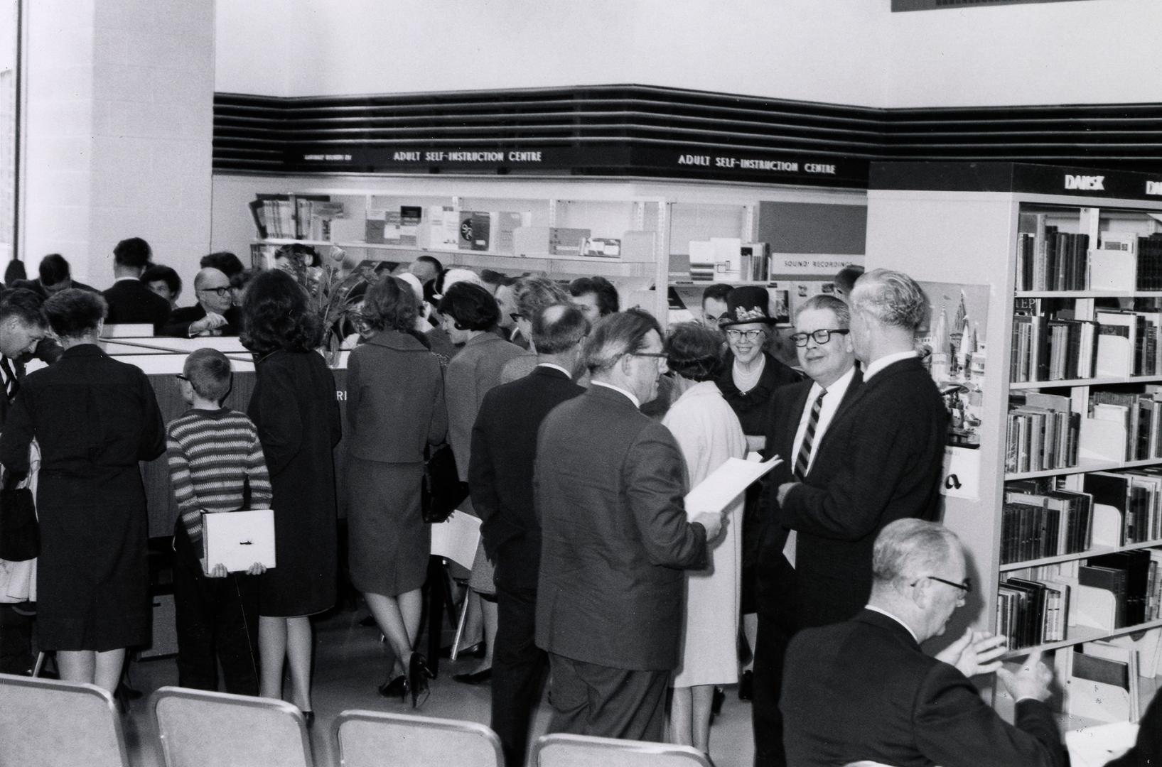 Picture of a crowd of people standing around in a library. 