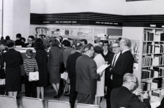 Picture of a crowd of people standing around in a library. 