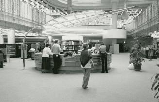 Picture of a round service desk with a canopy in a large library with customers in front and ba…