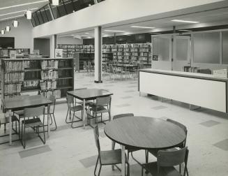 Picture of interior of a library showing study tables, service desk and shelves. 