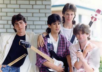 Four teen boys dressed shirts and casual blazers, one has drum sticks in pants waist band, two …