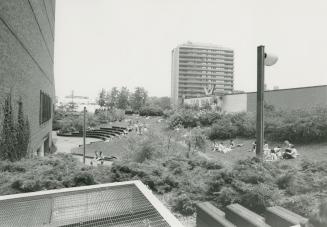Picture of library garden with amphitheatre seating and large apartment building in background.…