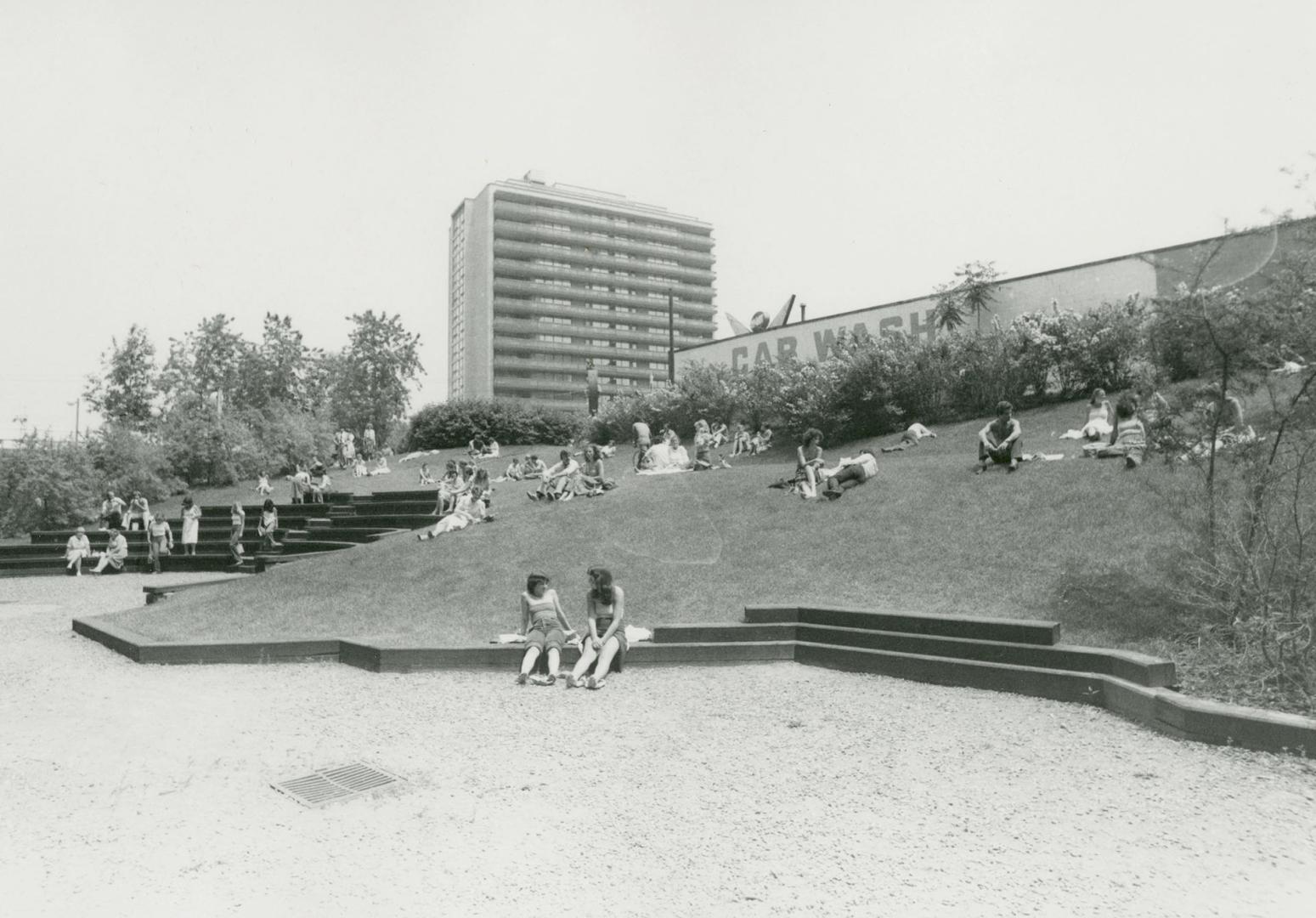 Picture of library garden with amphitheatre seating and large apartment building in background.…