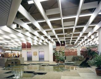Picture of 1970's library lobby with pond, elevator doors and prominent baffled ceiling. 
