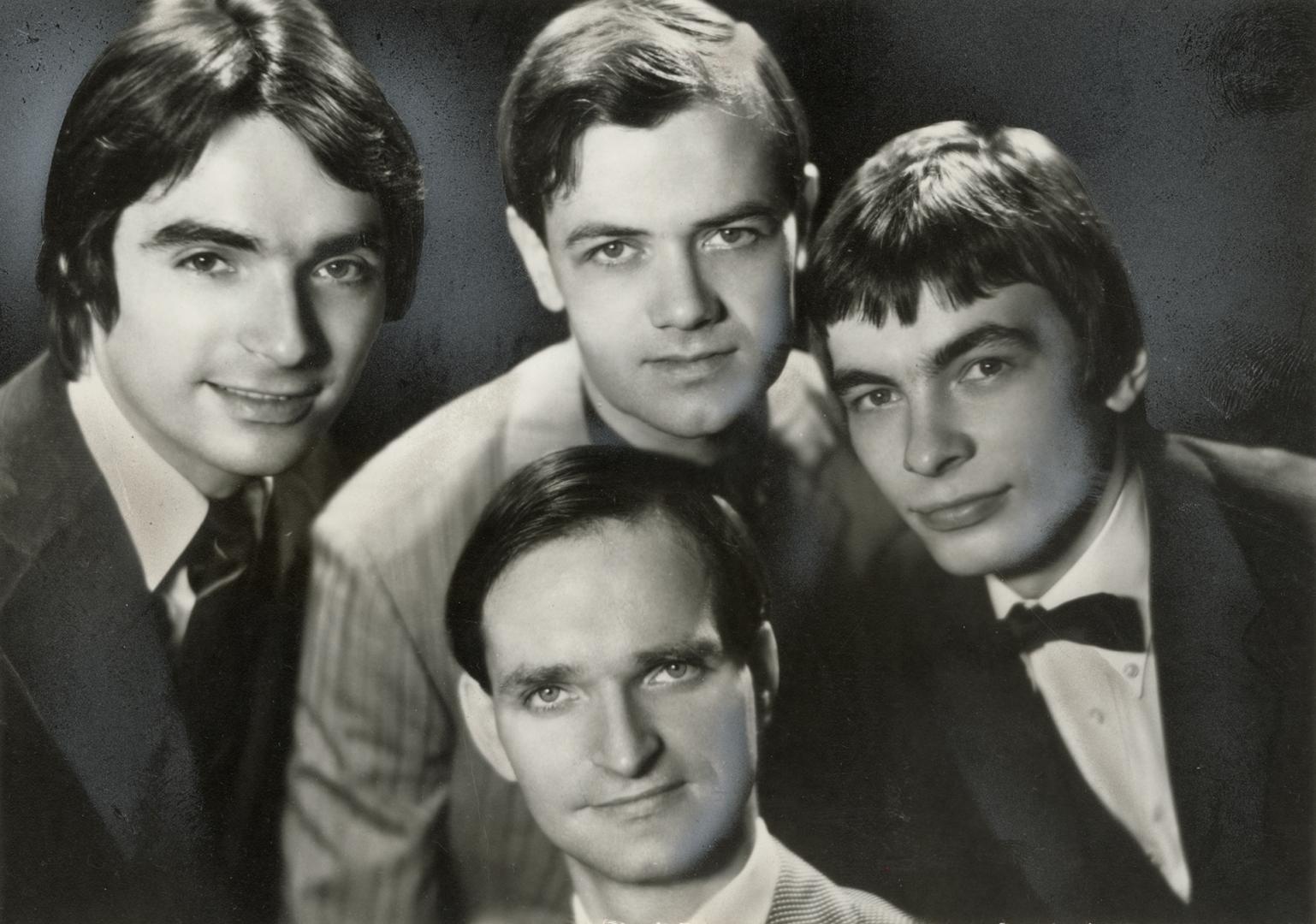 Four young in neatly cut hair and suits with shirt and ties situated in a cluster. 