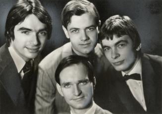 Four young in neatly cut hair and suits with shirt and ties situated in a cluster. 