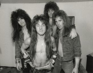 Two young men with big hair. One playing electric guitar and the other with his arm around the …