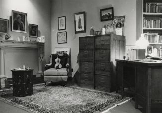 Victorian style room with large Persian rug, desk with books, vertical files, a chair with a vi…