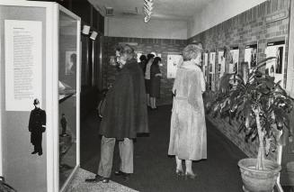 A man and a woman stand back to back in a gallery showcasing materials from the Toronto Public …