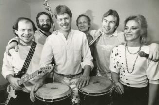 five men and a woman on the far right in a row with guitars and bongos. 