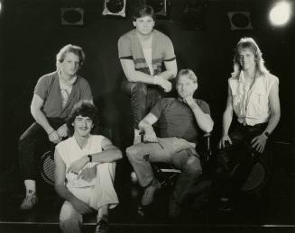 Five young on darkened stage with lights above sitting in various casual dress, t-shirts and je…