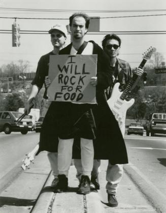 Three young men wearing light coloured jeans on Street car tracks during sunny day. Front man c…