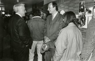 A women and two men gathered facing each other in conversation. Behind them are images on the w…