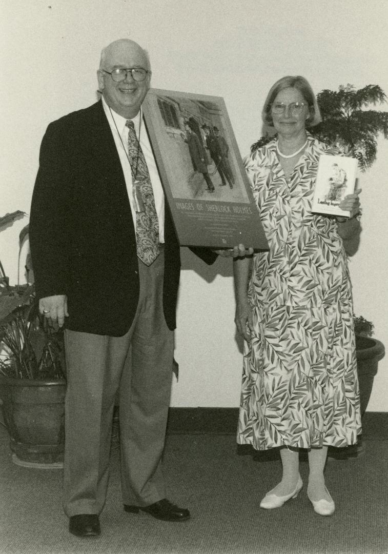Black and white photograph of man and woman stand side. Man hold poster of gallery opening, wom…