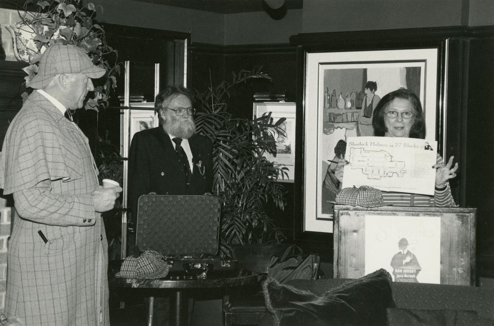 Black and white photograph. Three figures standing my a podium. Woman to the left stands behind…