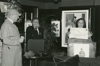 Black and white photograph. Three figures standing my a podium. Woman to the left stands behind…
