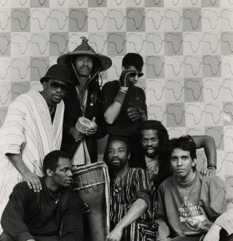  A group of seven young men sitting and standing against outline of Africa wallpaper, casually …