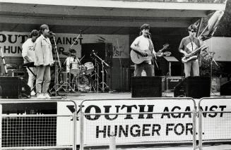 A band performing on stage. There is a banner stating Youth against hunger for...