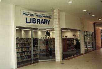 Picture of the front of glassed walls of a library that is inside a mall. 