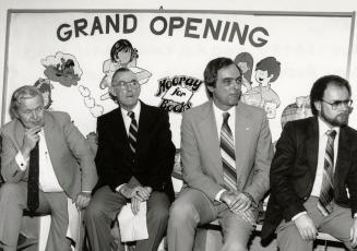 Picture of four men sitting in front of a sign that says "grand opening". 