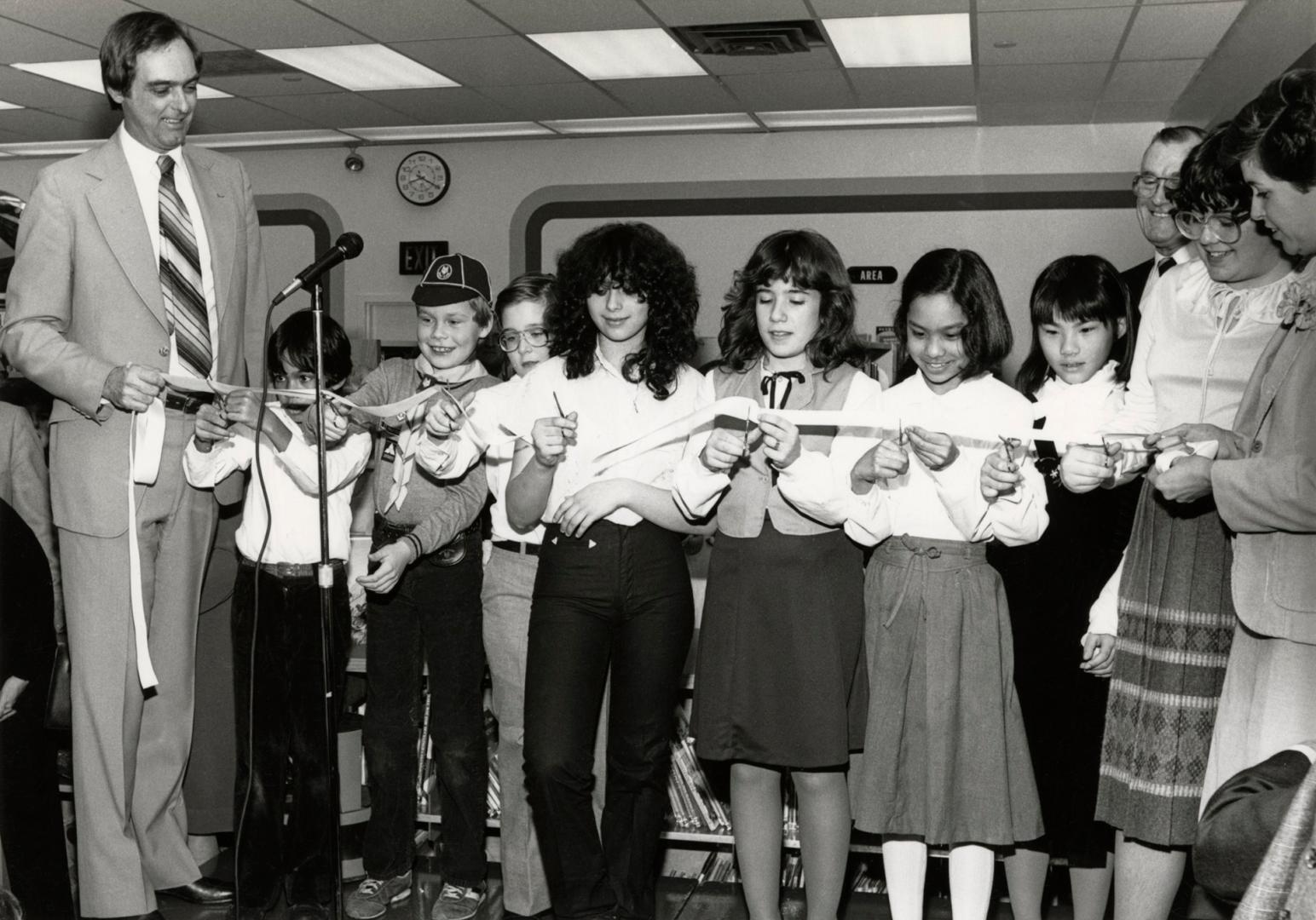 Picture of man on left holding a long ribbon and row of children holding it and getting ready t…