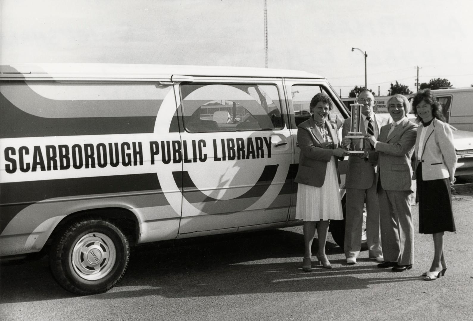 Picture of 4 people holding a trophy and standing in front of a Scarborough Public Library van.