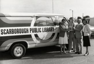 Picture of 4 people holding a trophy and standing in front of a Scarborough Public Library van.
