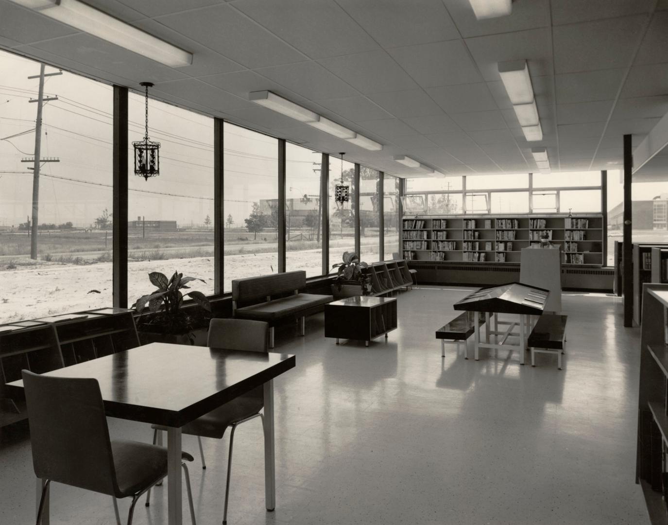 Picture of a 1950's library interior showing tables, couch and shelving and large glass windows…