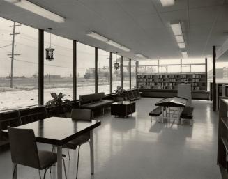 Picture of a 1950's library interior showing tables, couch and shelving and large glass windows…