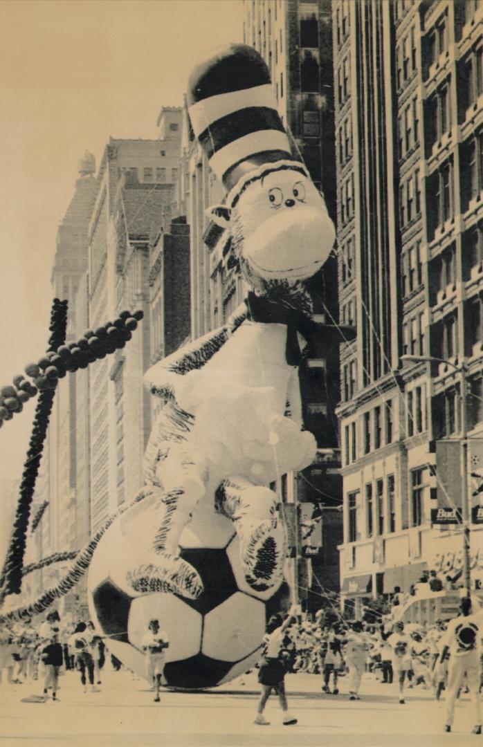 A 7 story balloon depiction of of tall slender cat with striped top cat on top of a gigantic so…