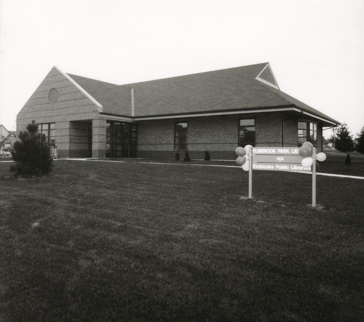 Picture of a one storey library building with peaked roof and large lawn in front. 