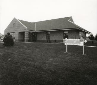 Picture of a one storey library building with peaked roof and large lawn in front. 