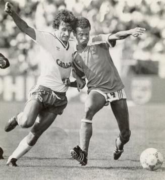 Canada's soccer player Paul James runs toward the ball while France's Jean Tigana (r) grabs his…