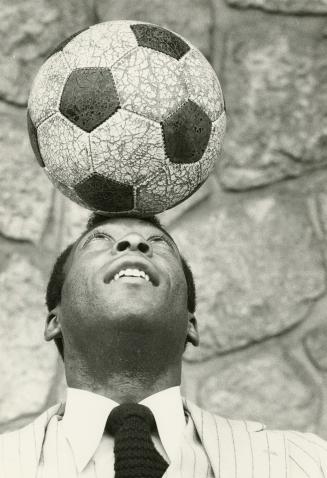 Head and shoulders of man in suit and tie balancing a soccer ball on the top of his forehead. 