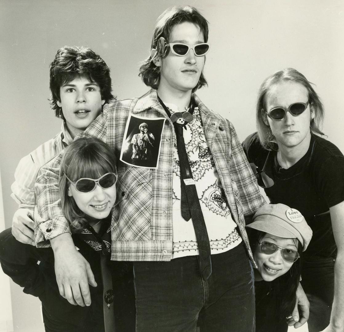 Five young people: one standing in the centre and two flanking him on either side. girls below …