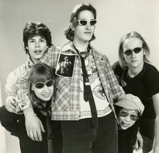 Five young people: one standing in the centre and two flanking him on either side. girls below …
