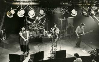 Looking down on the stage, from left, singing woman, male sax player in patterned suit, and mal…