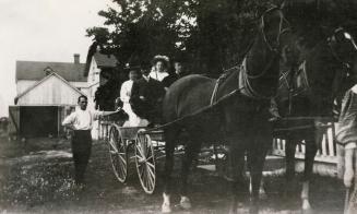 Picture of horses and wagon with people in wagon and man standing beside it. 