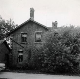 Picture of a two storey farmhouse partly covered with large bushes. 