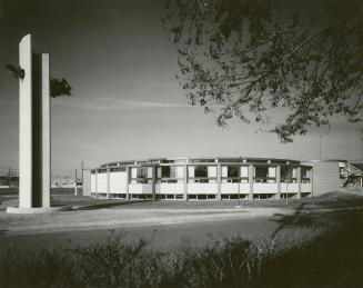 Picture of a 1960s one storey round library building with tower to the left and lawn and tree i…