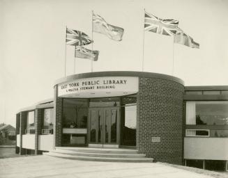 Picture of a 1960s one storey round library building with five flags on top. 
