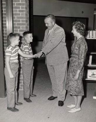 Picture of a man shaking the hands of twin boys while a woman looks on. 