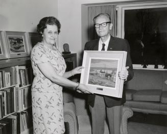 Picture of a man and a women holding a framed painting. 
